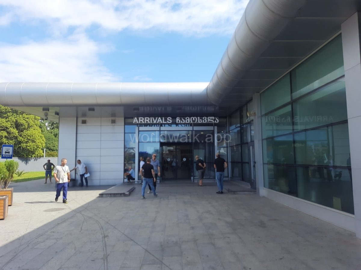 Arrivals exit at Batumi Airport with travellers and a taxi sign visible outside