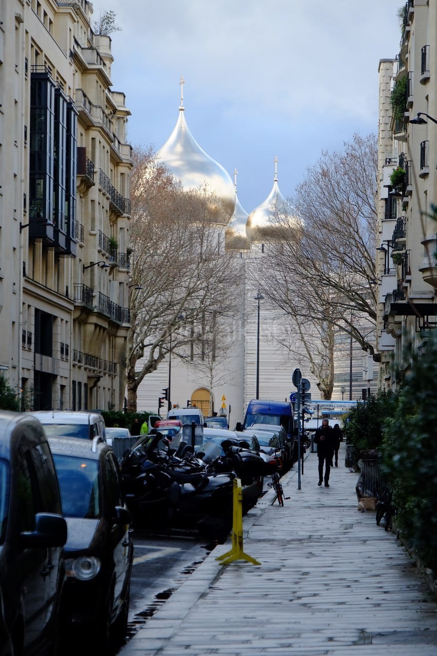A residential Paris street with parked scooters near a church tower